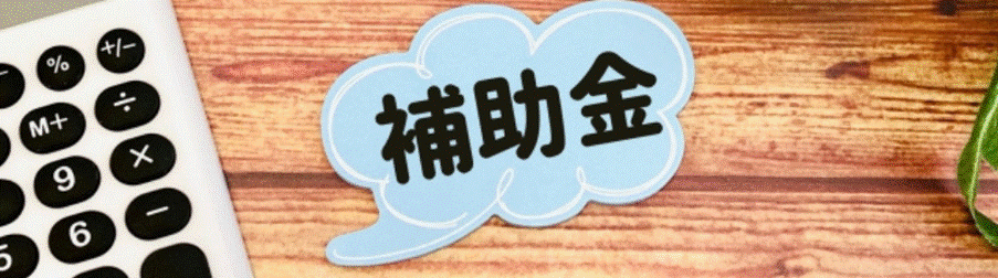 木目の机の上に置かれた吹き出し型の「補助金」メモと電卓のイメージ