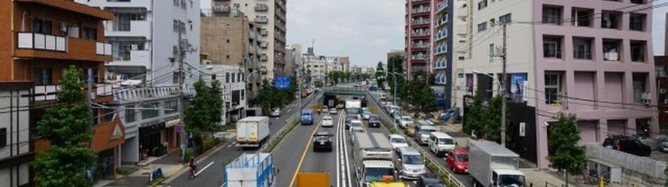 都市部の幹線道路を走る車両やトラックが映る交通量の多い通りの様子
