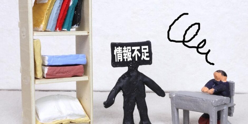 情報不足と書かれた黒い粘土人形と机に座る人物のミニチュア