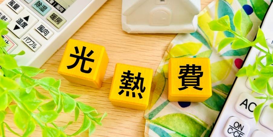 電気・ガス代を示す「光熱費」の文字と家のオブジェ、エアコンリモコンが並ぶ節約のイメージ