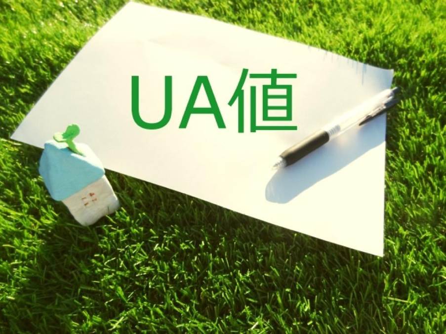 芝生の上に置かれた「UA値」の紙と小さな家のオブジェ、省エネ指標のイメージ
